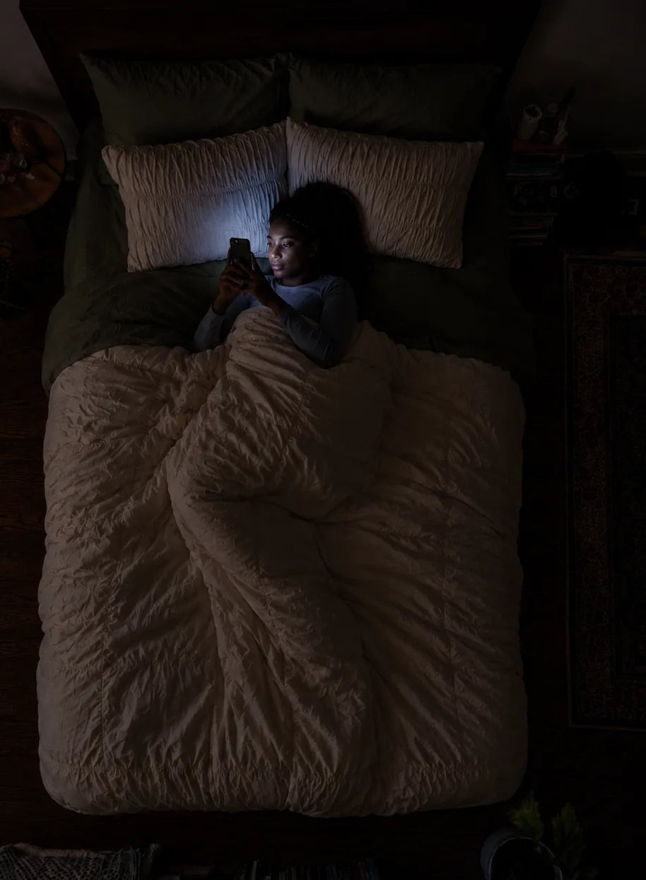 Eine Frau scrollt nachts im Bett am Handy, das Display beleuchtet ihr Gesicht