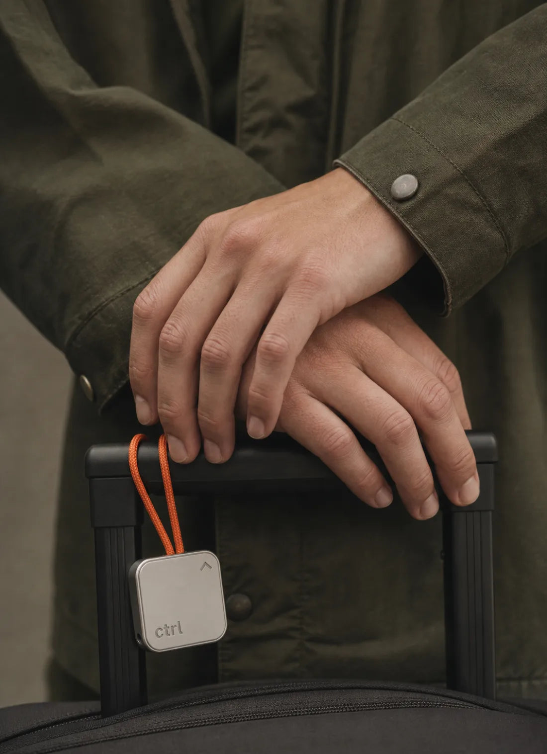 Gekreuzte Hände auf einem Koffergriff, der ctrl key hängt an einem Band